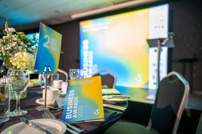 Formal event setup with Business Awards 2025 program on dining table and presentation screens.